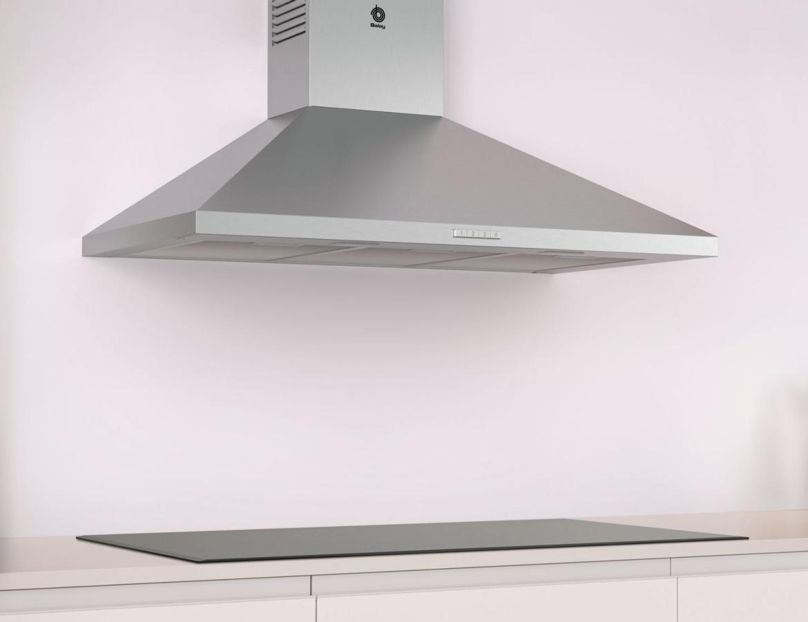 Campana extractora de acero inoxidable sobre una placa de cocina de vidrio en una superficie y pared blancas.