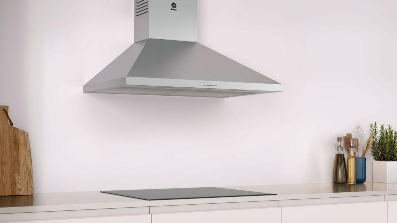 Una escena de cocina con una campana extractora de acero inoxidable sobre una placa de inducción. Debajo, gabinetes blancos.