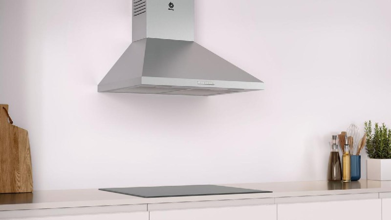 Campana extractora de acero inoxidable sobre encimera clara. Pared blanca y mueble de cocina blanco.