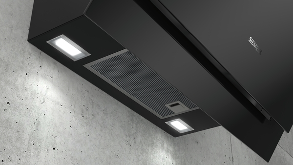Schwarze Dunstabzugshaube an einer Betonwand. Zwei Lichter sind an. Siemens-Logo.