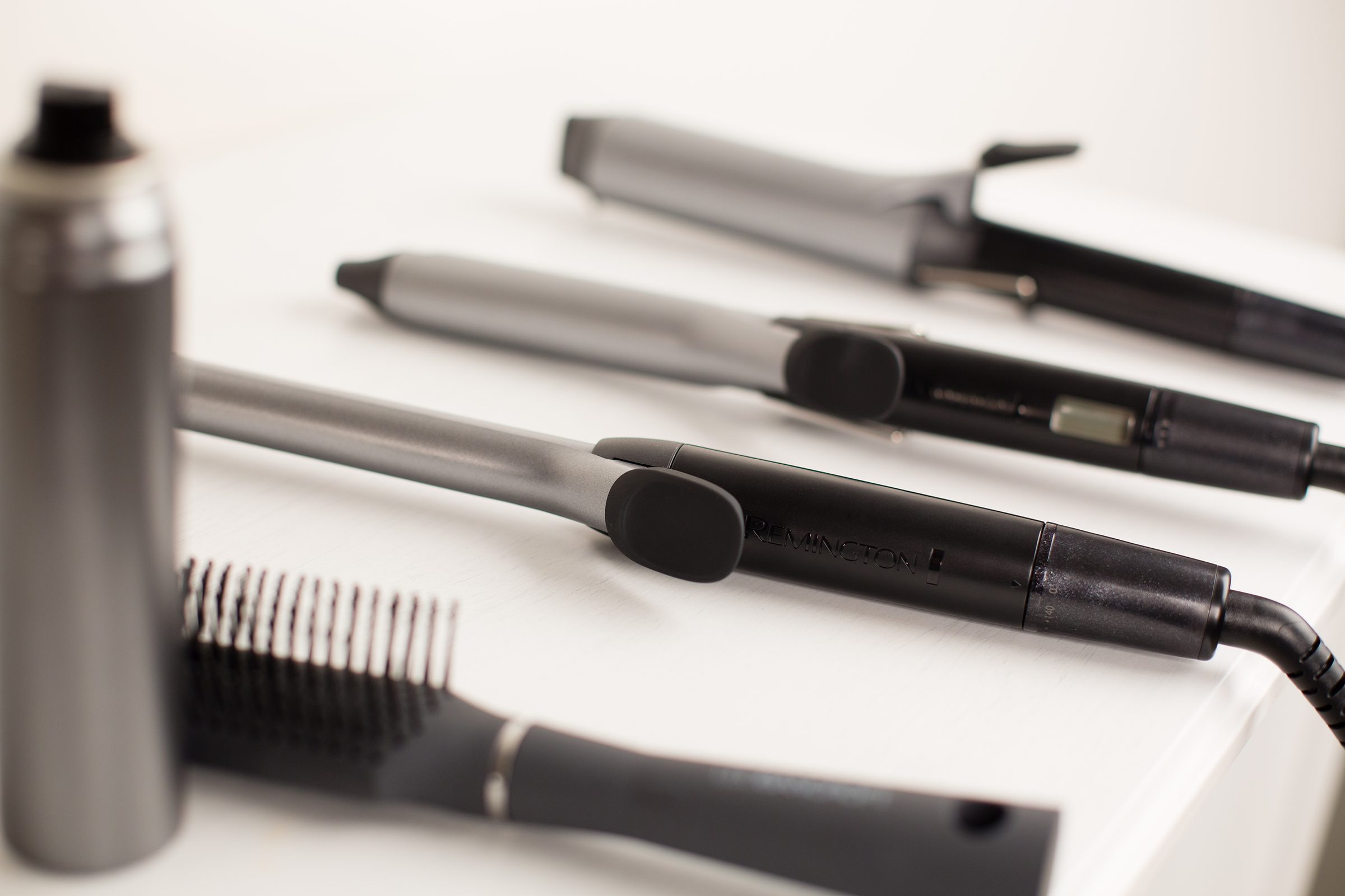 Haarstylingtools: verschillende krultangen, een borstel en een fles haarlak op een wit oppervlak.