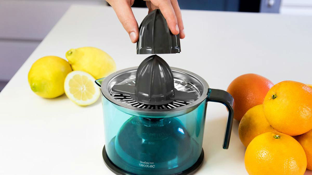 Una mano coloca la parte superior de un exprimidor de cítricos sobre la base, con limones y naranjas.