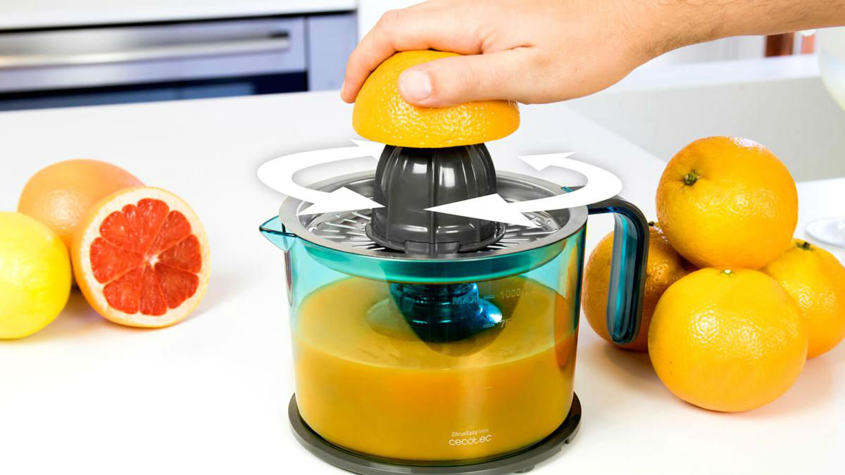 Una persona exprimiendo una naranja con un exprimidor manual, con naranjas y pomelos alrededor.