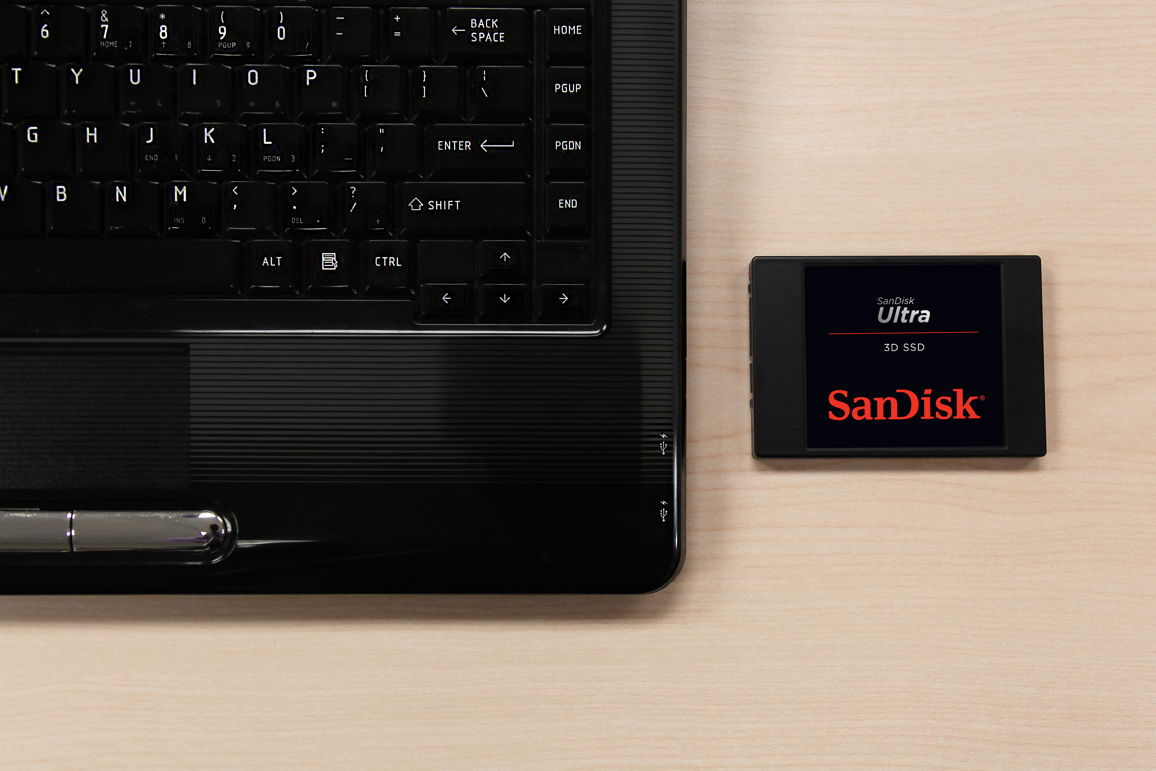 Ein Laptop und eine SanDisk Ultra 3D SSD liegen auf einer Holzoberfläche.