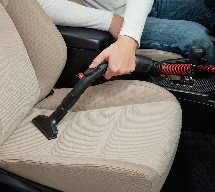 Een persoon die een autostoel stofzuigt met een kleine stofzuiger.