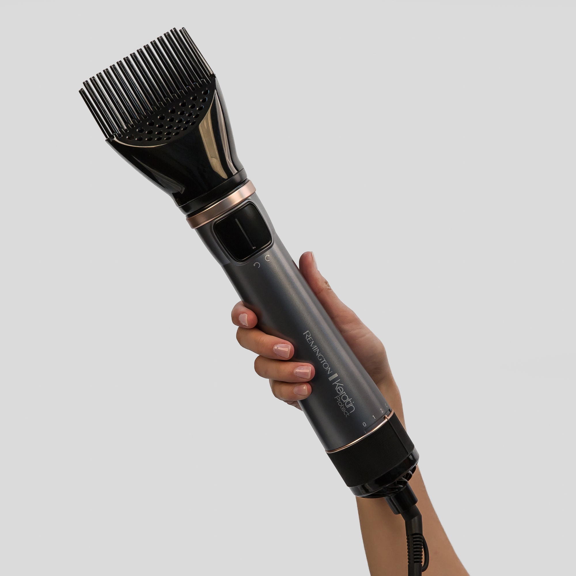 A woman's hand holding a Remington Keratin Protect hair dryer brush against a white backdrop.