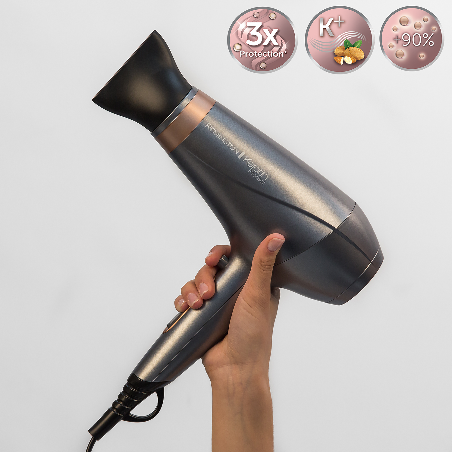 A hand holding a grey and rose gold Remington Keratin Protect hair dryer.