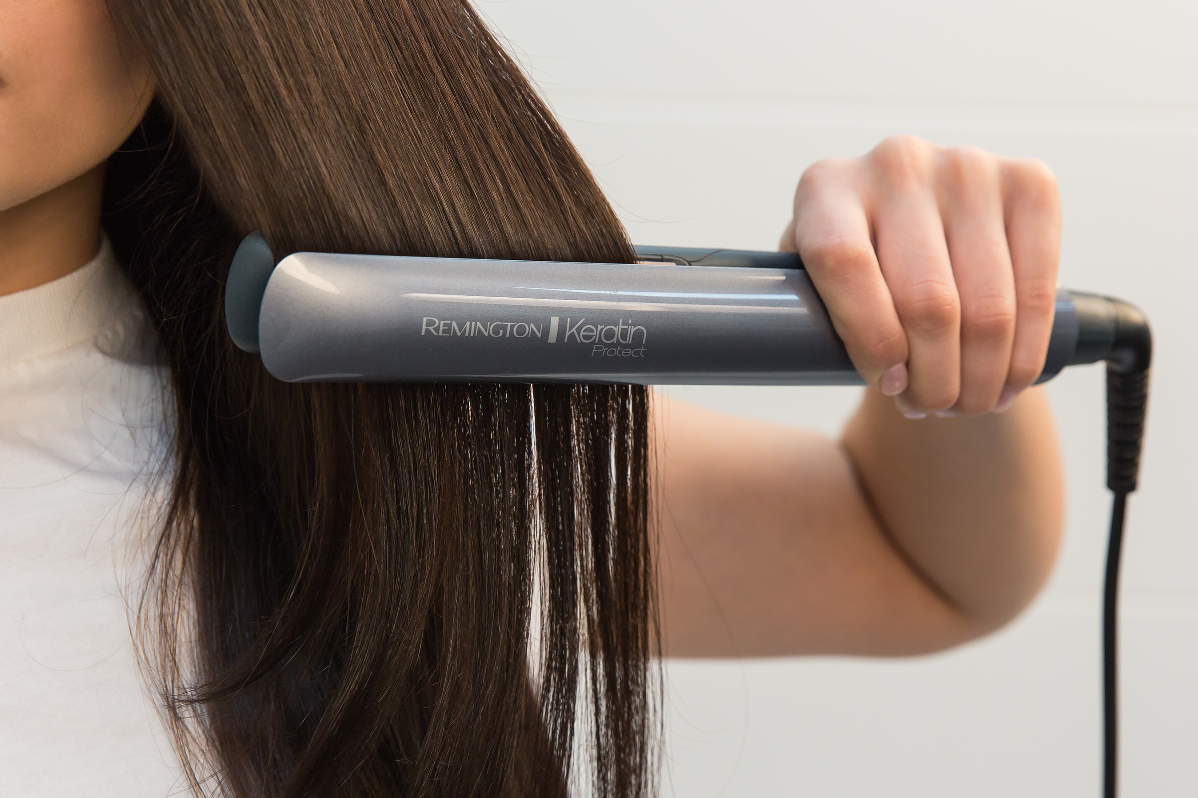 Vrouw die haar steilt met een grijze Remington Keratin Protect stijltang.