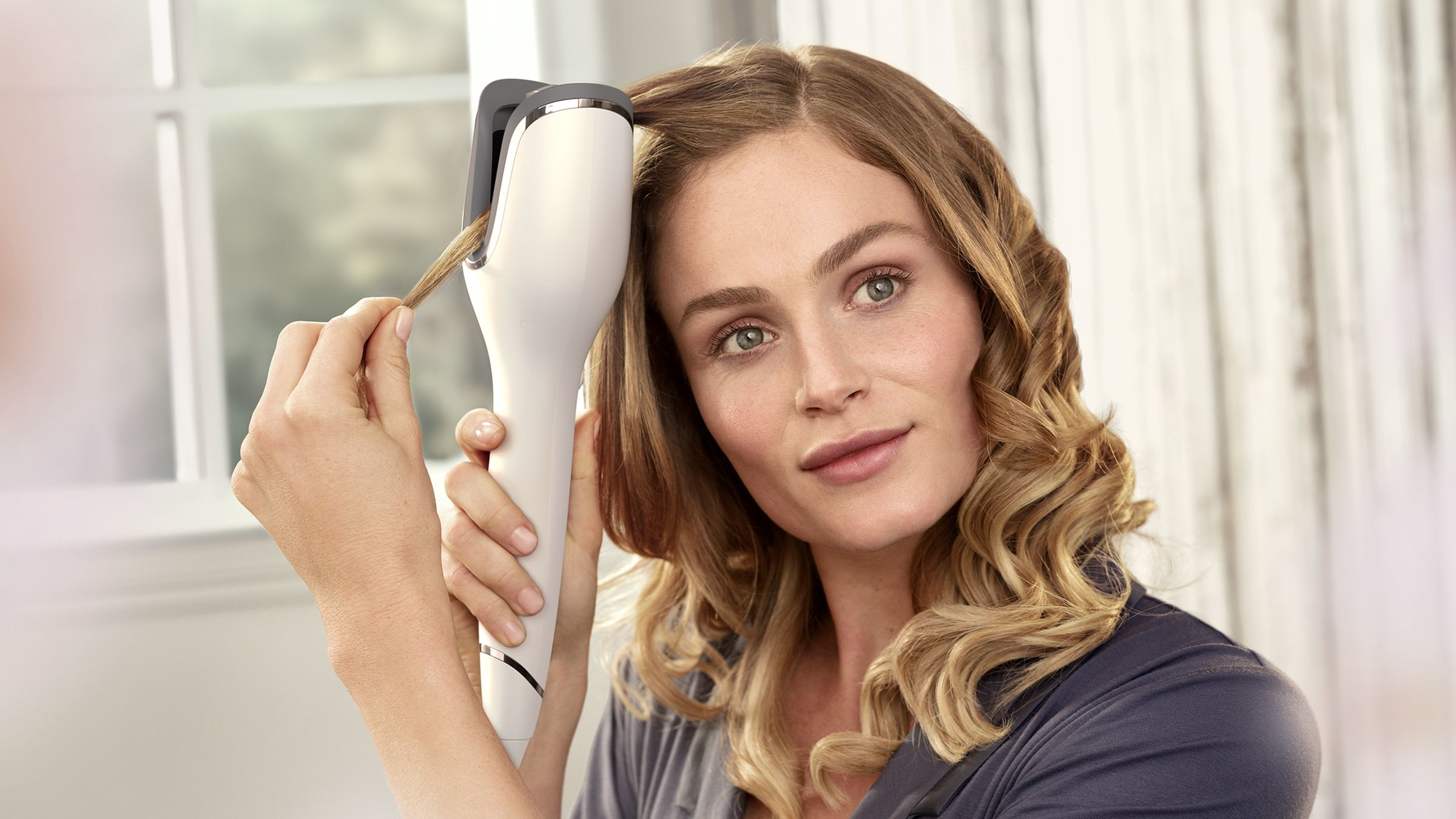 Donna con arricciacapelli che si acconcia i capelli, tiene l'utensile.