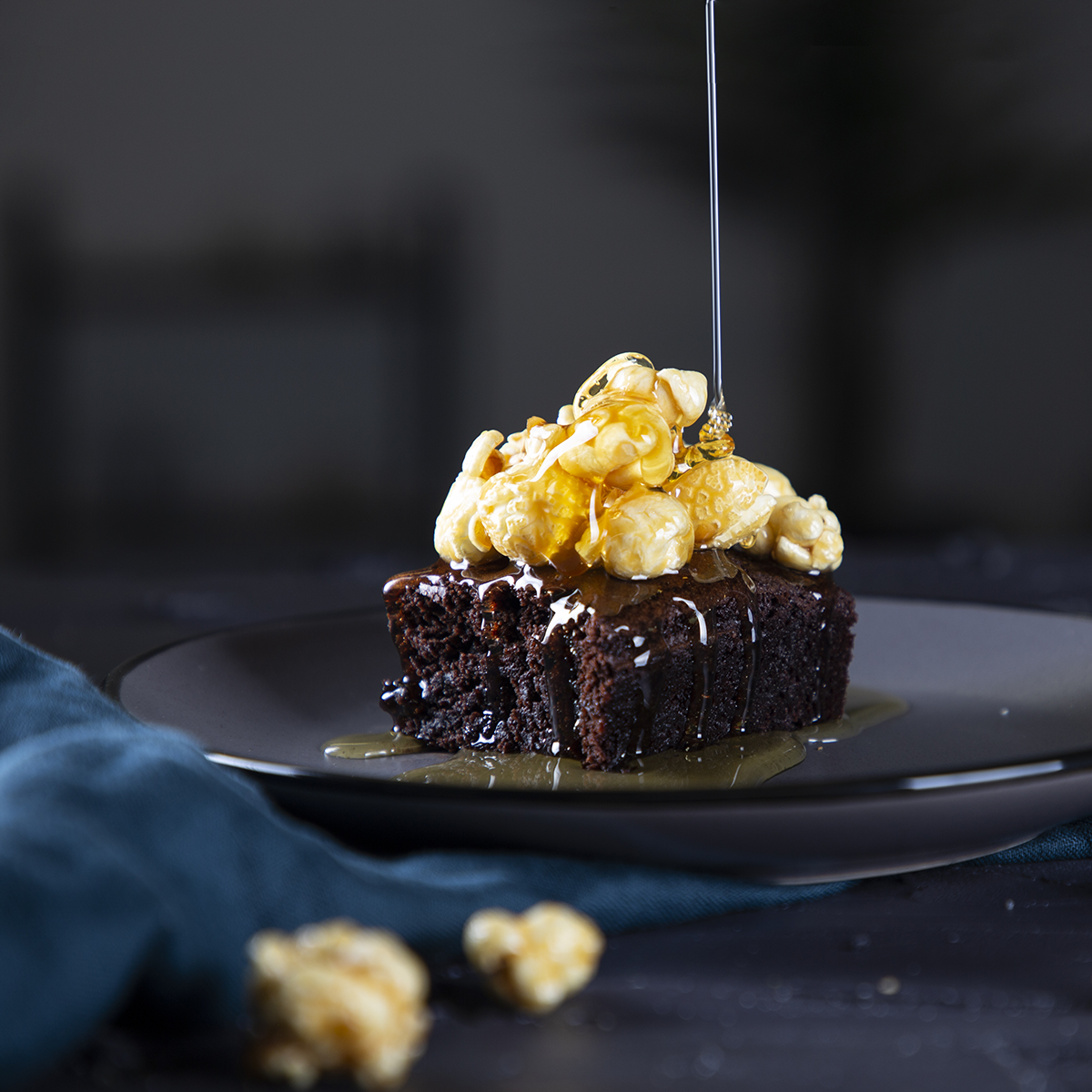 Brownie met popcorn topping en honing die eroverheen wordt gesprenkeld op een donker bord.