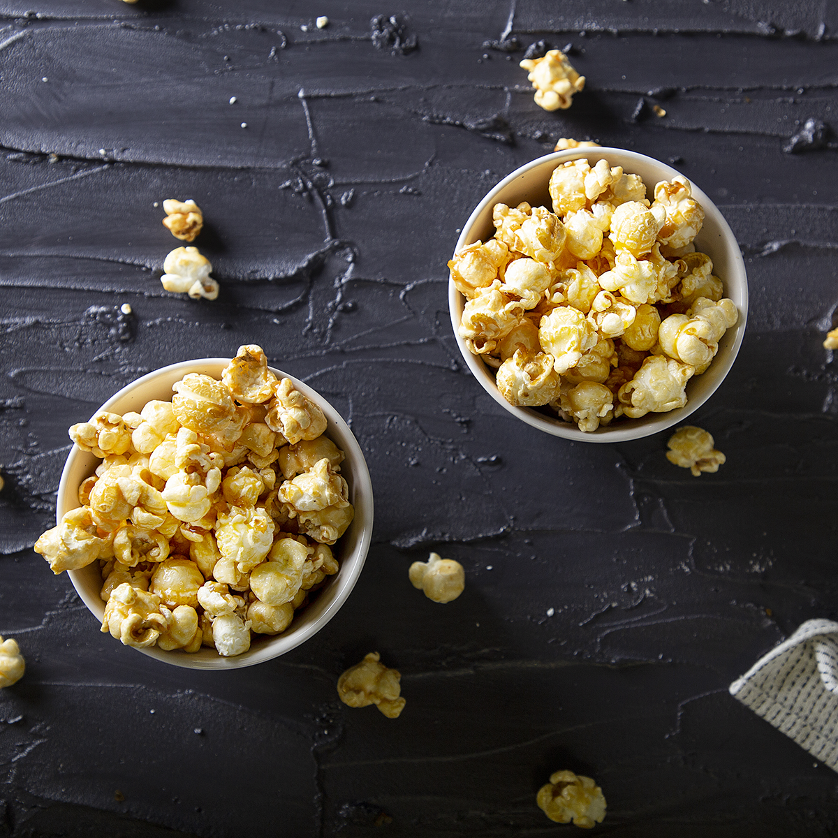 Twee kommen popcorn op een zwart oppervlak. De popcorn is met karamel bedekt.