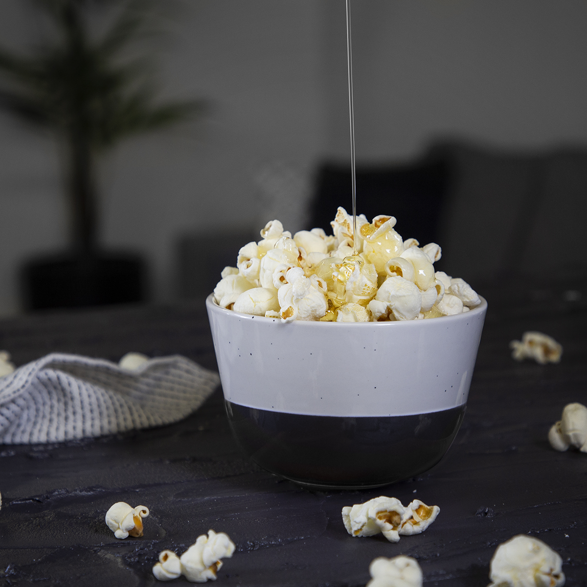 Een kom popcorn met karamel eroverheen gegoten op een donker oppervlak met wat verspreide popcorn.