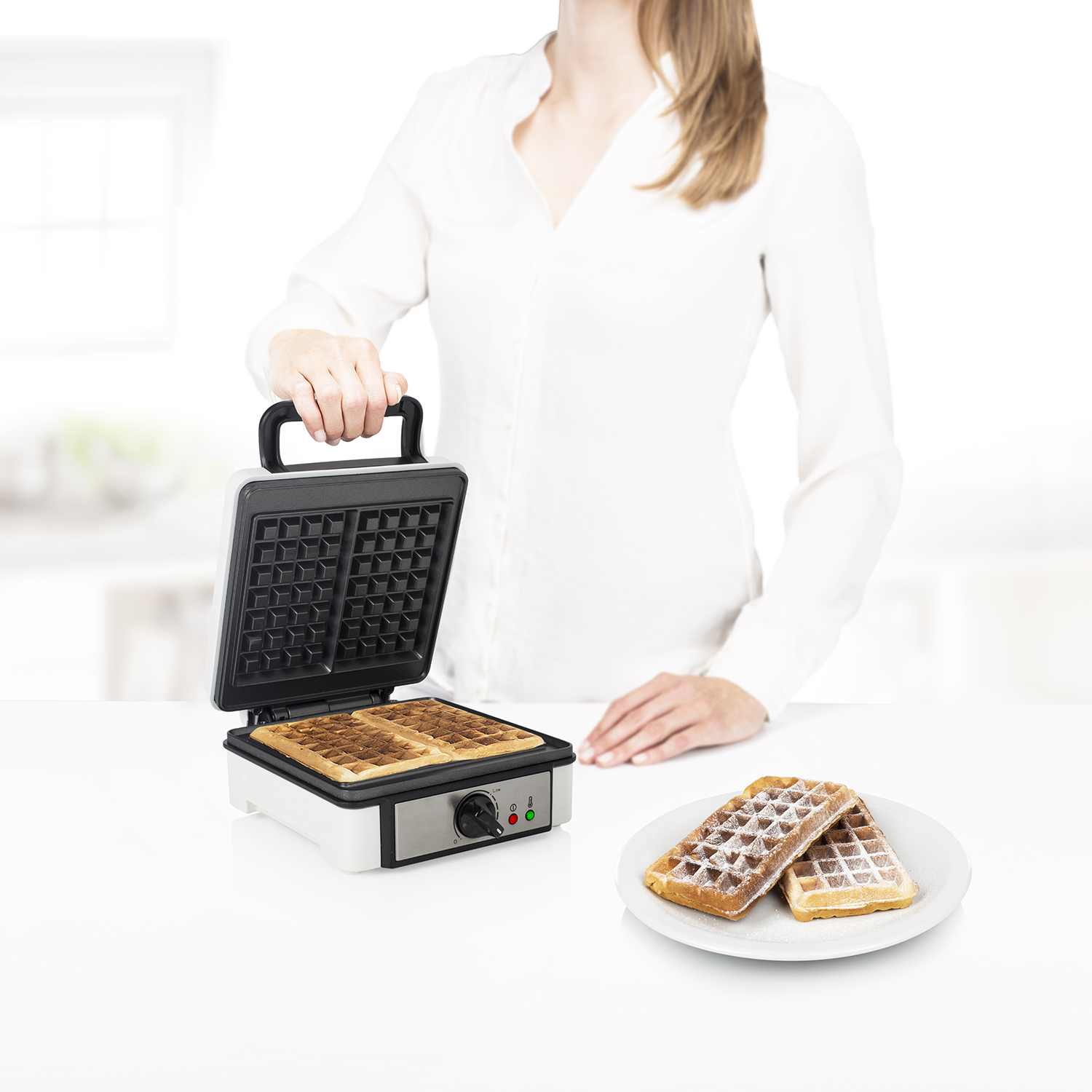Een persoon die een wafelijzer vasthoudt met wafels en poedersuiker op een bord.