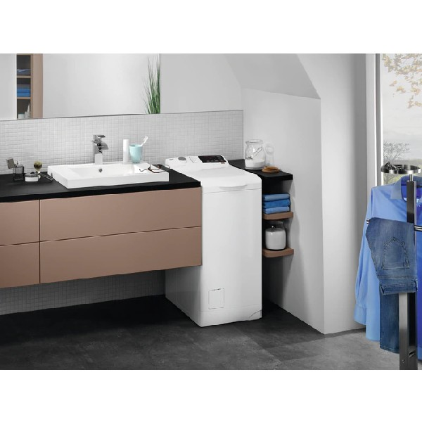 Lavadora de carga superior AEG blanca en un baño con lavabo y estantes.