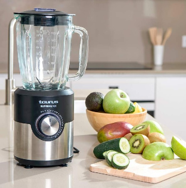 Licuadora con fruta. La licuadora es negra y plateada. Las frutas incluyen manzanas, mangos y kiwi.