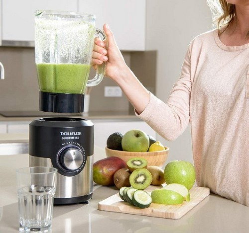 Una mujer preparando un batido con una licuadora, frutas y verduras en una encimera de cocina.