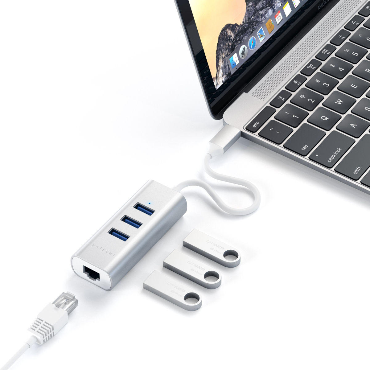 Un hub Satechi argenté est connecté à un ordinateur portable avec des clés USB à proximité et un câble Ethernet.