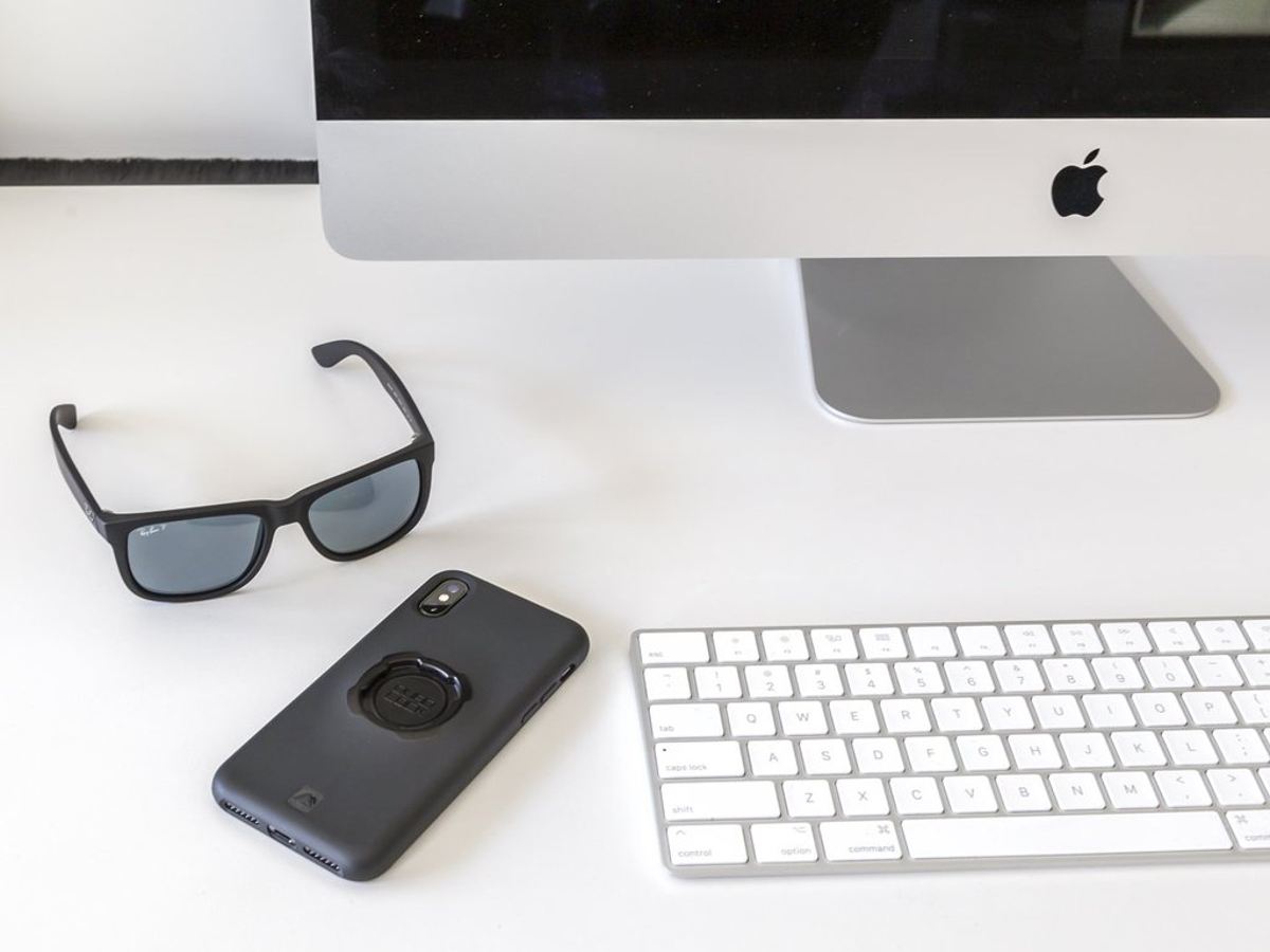 Schreibtisch mit Sonnenbrille, Telefon, Tastatur und Monitor mit Apple-Logo.