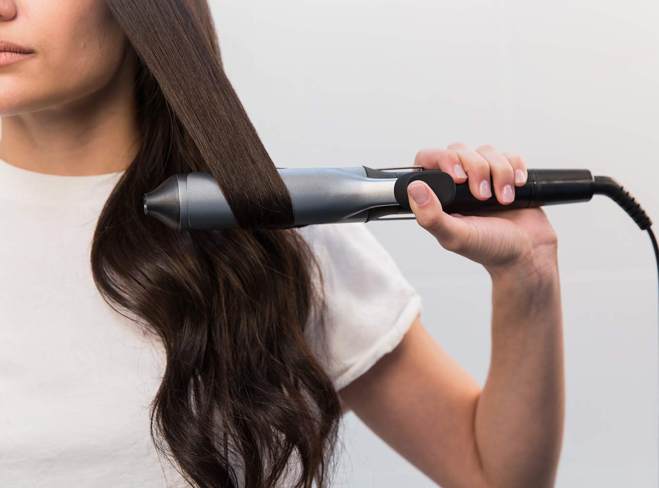 A woman straightening her dark hair with a gray hair straightener.