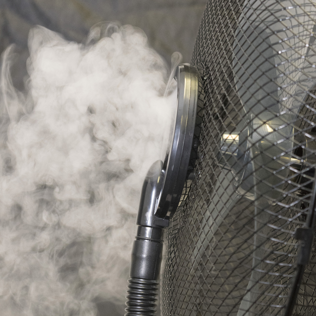 Egy fekete ventilátor fehér gőzt fúj. A ventilátor sötétszürke háttér előtt van.