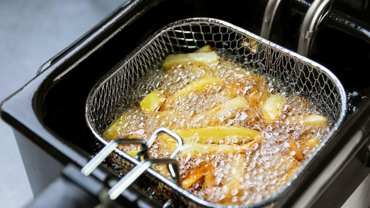 Patatas fritas en una cesta de alambre, sumergidas en aceite caliente dentro de una freidora.