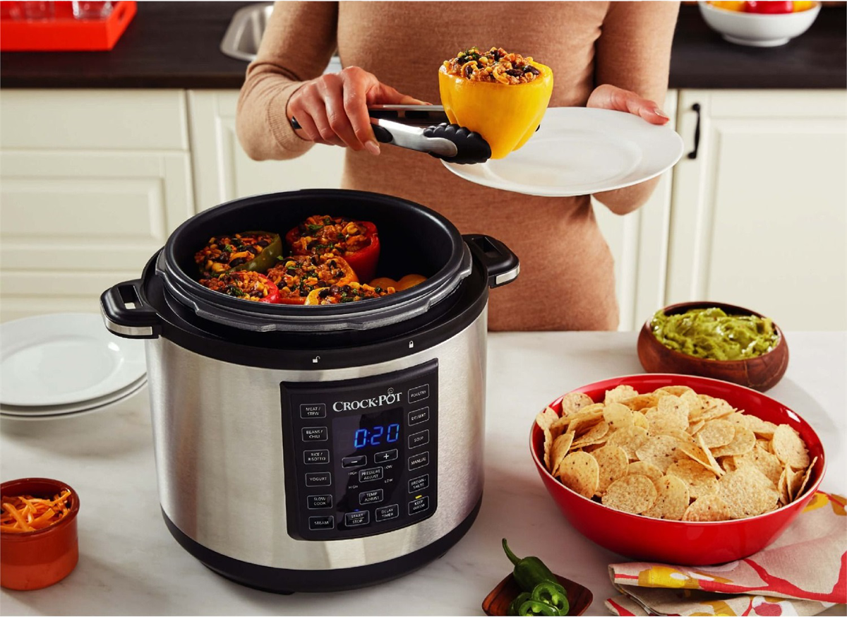 Une femme utilise des pinces pour retirer un poivron farci d'un Crock-Pot. D'autres poivrons, chips et guacamole sont sur le comptoir.