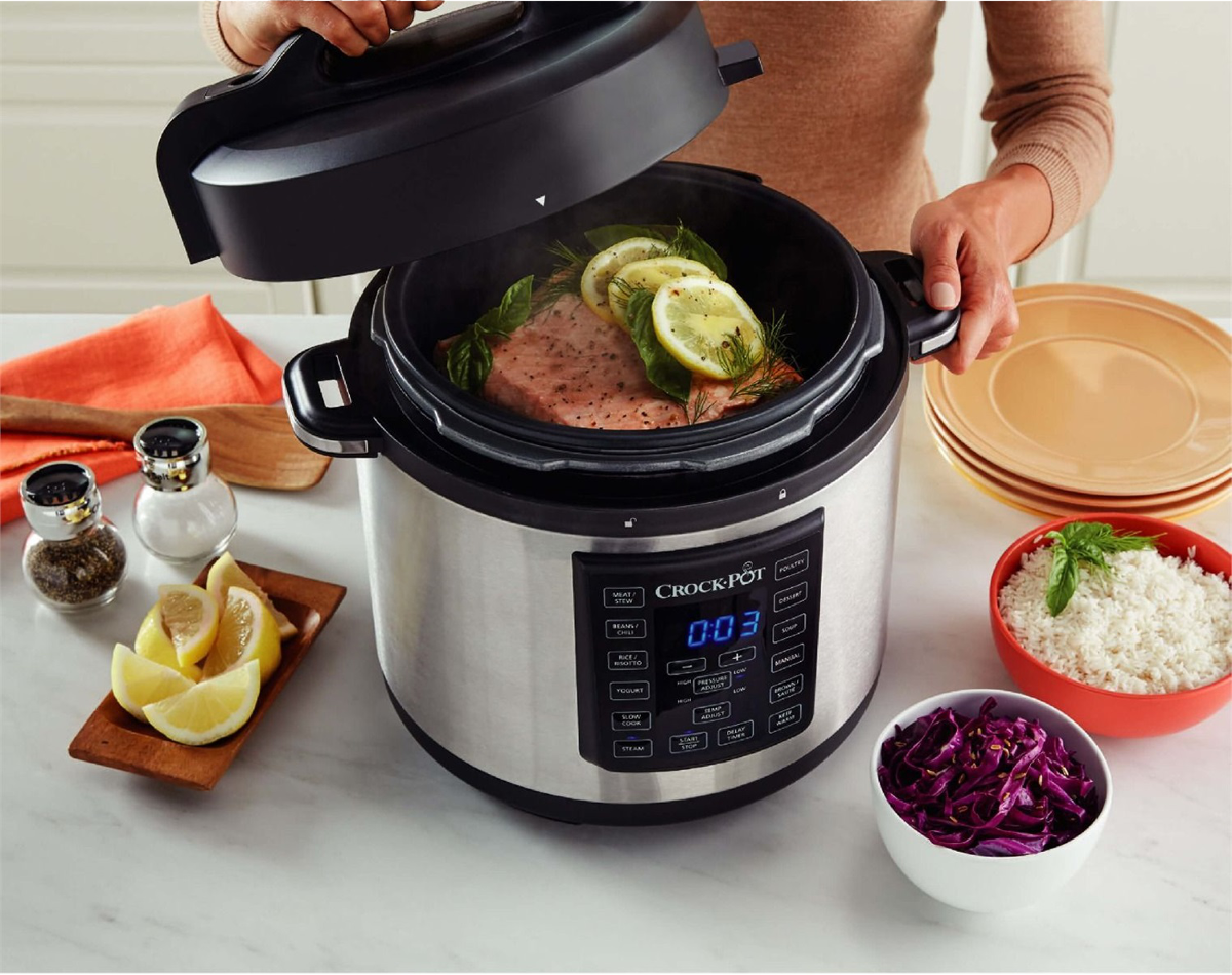 Une personne ouvrant un Crock-Pot avec de la nourriture à l'intérieur. Le pot a un affichage numérique et les côtés sont visibles.