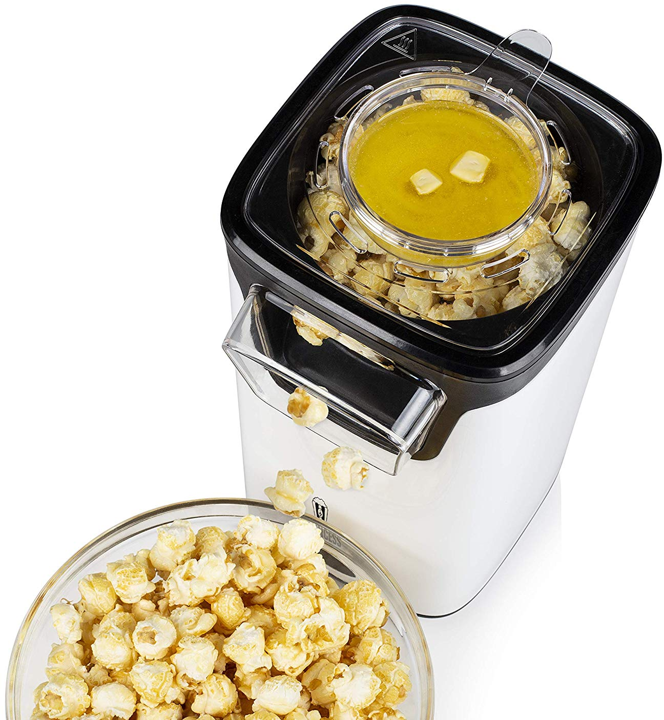 Una macchina per popcorn con mais scoppiettante e burro fuso. Una ciotola di popcorn in primo piano.