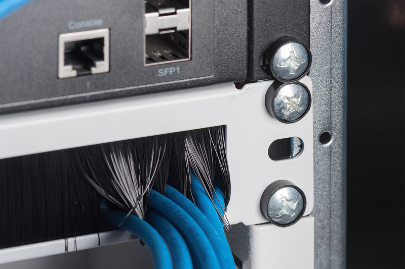 Nahaufnahme eines Netzwerkgeräts. Blaue Kabel und Anschlüsse. Schrauben und ein schwarzer Rahmen sind sichtbar.