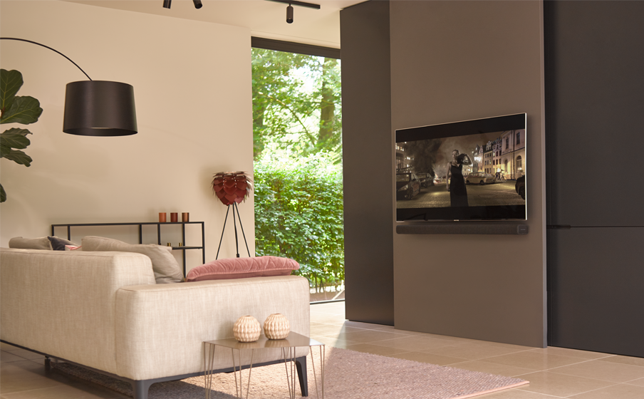 Woonkamer met een tv aan de muur, een bank, een kleed en een deur.