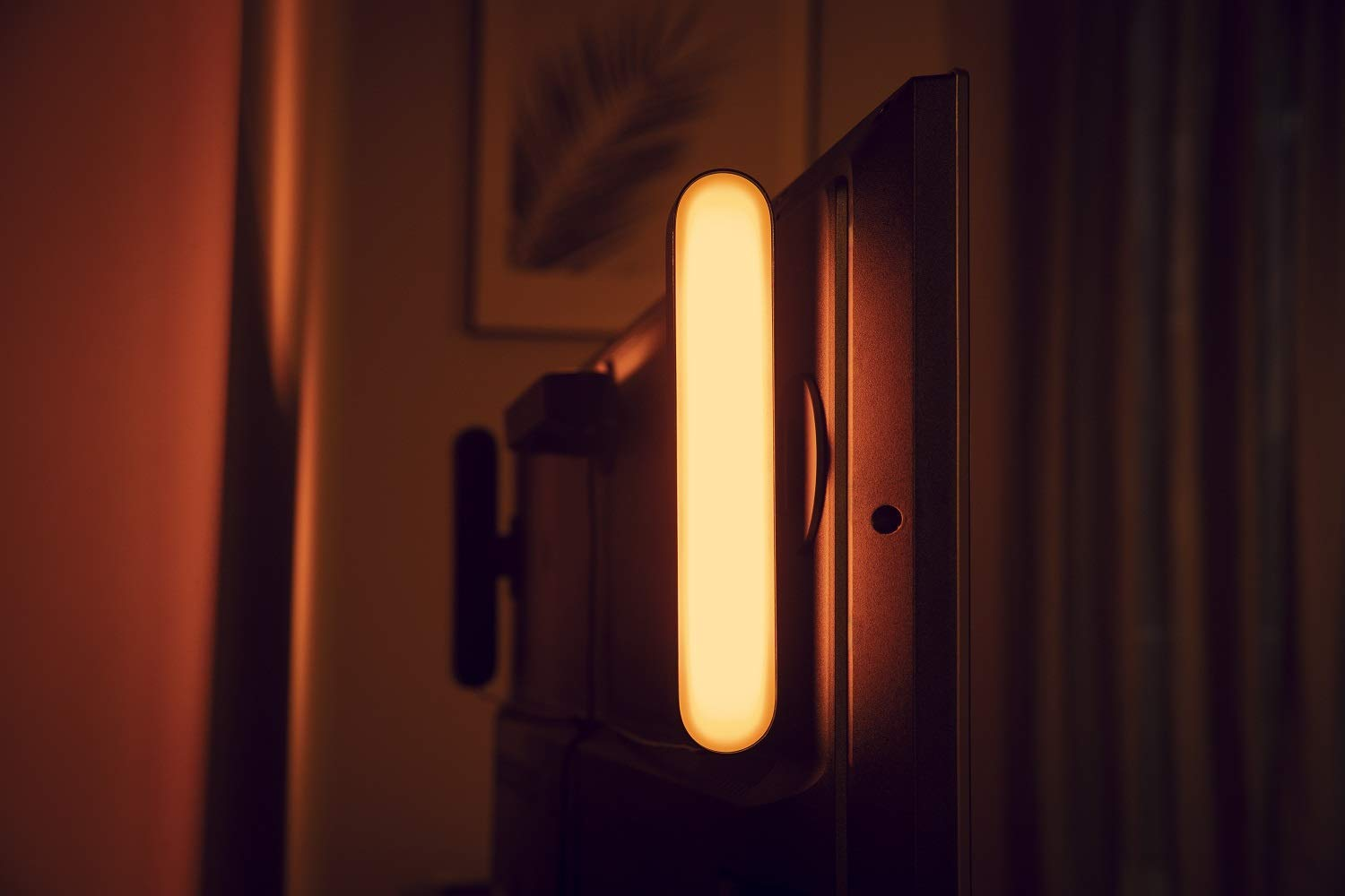 Una tira de luz adjunta a un televisor, emitiendo luz cálida en una habitación oscura, vista lateral.