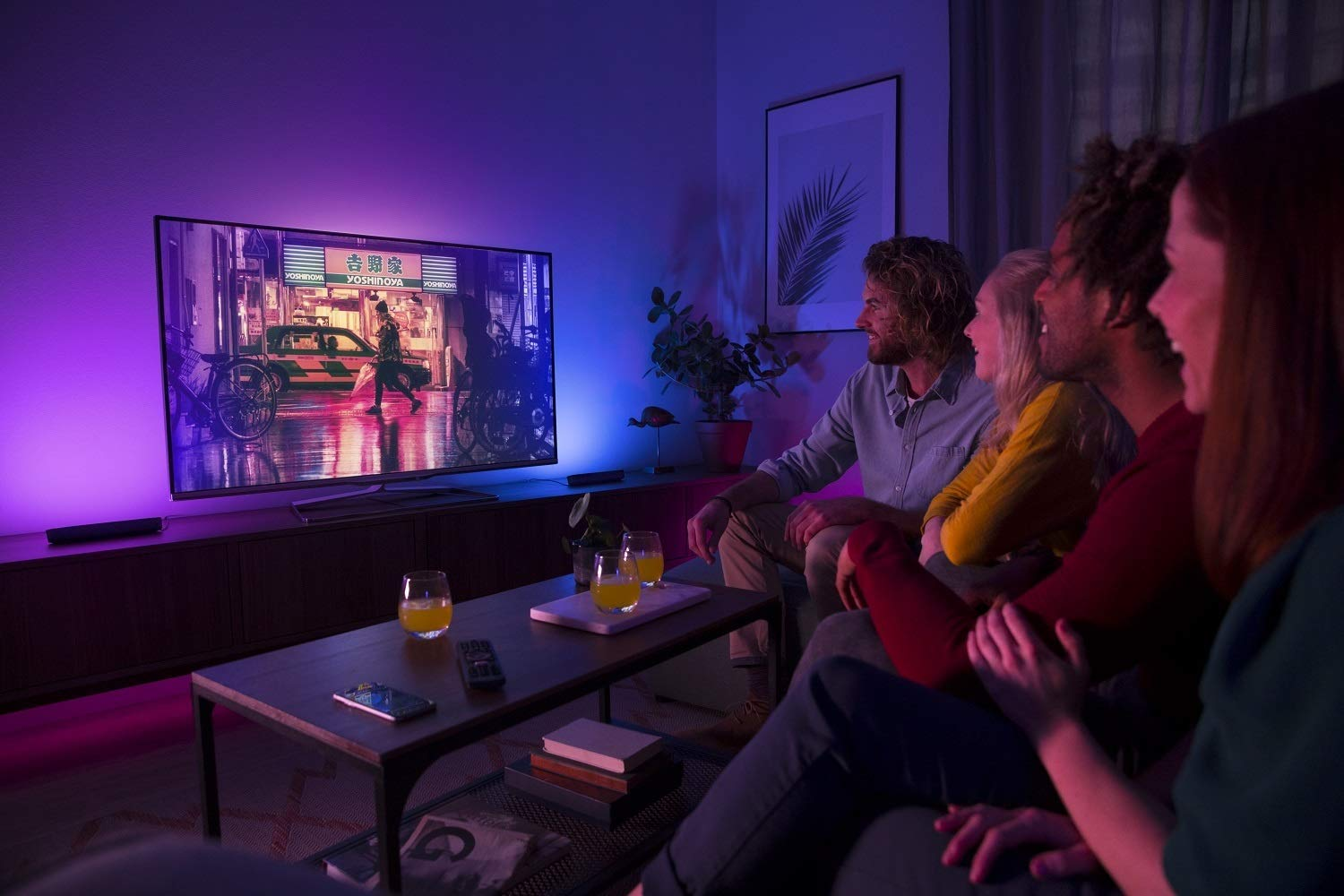 Grupo de personas viendo la TV. La TV muestra una escena callejera nocturna. Luces de colores.