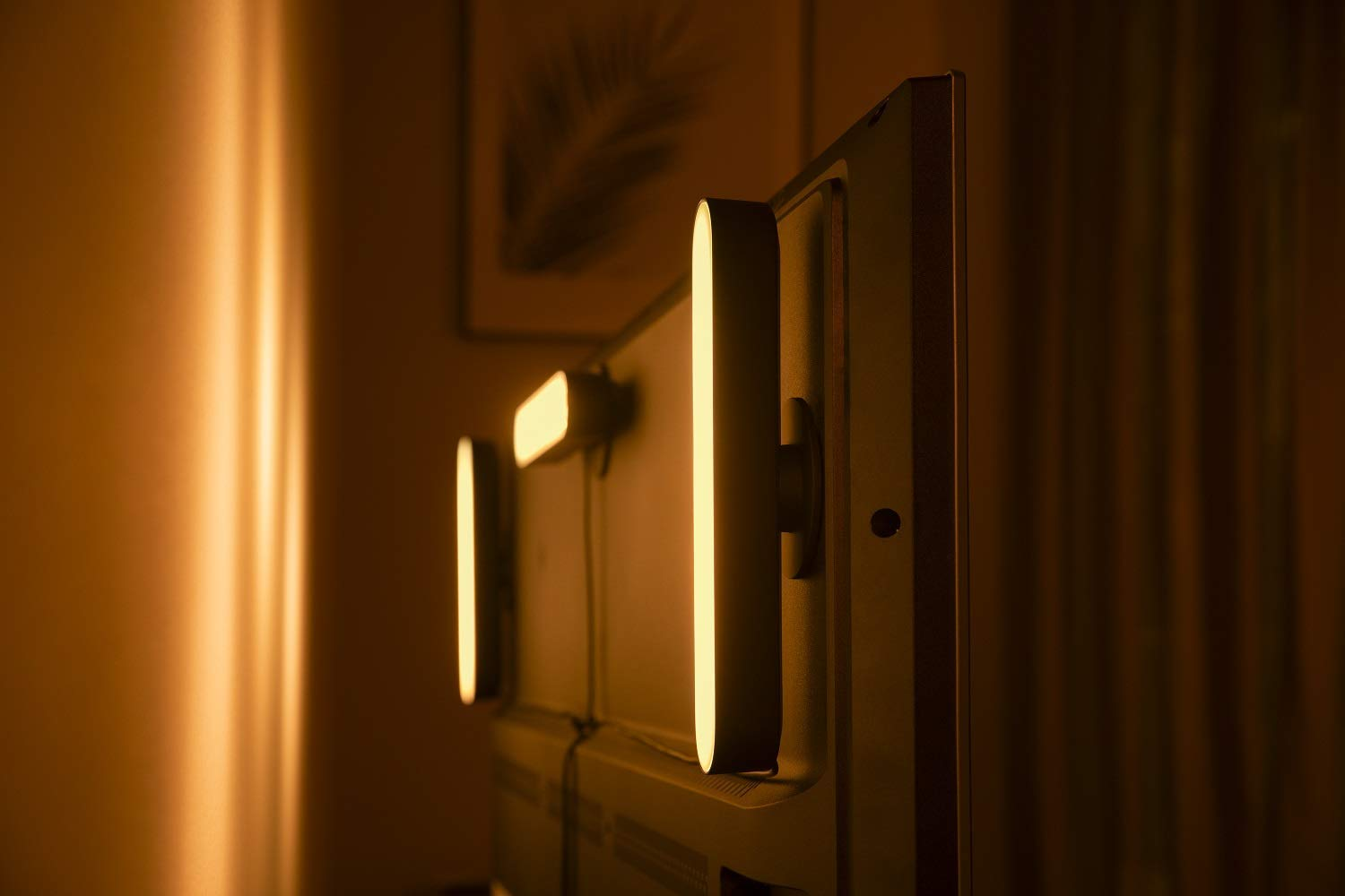 Tres barras de luz unidas a la parte posterior de un televisor, creando un brillo cálido y ambiental.