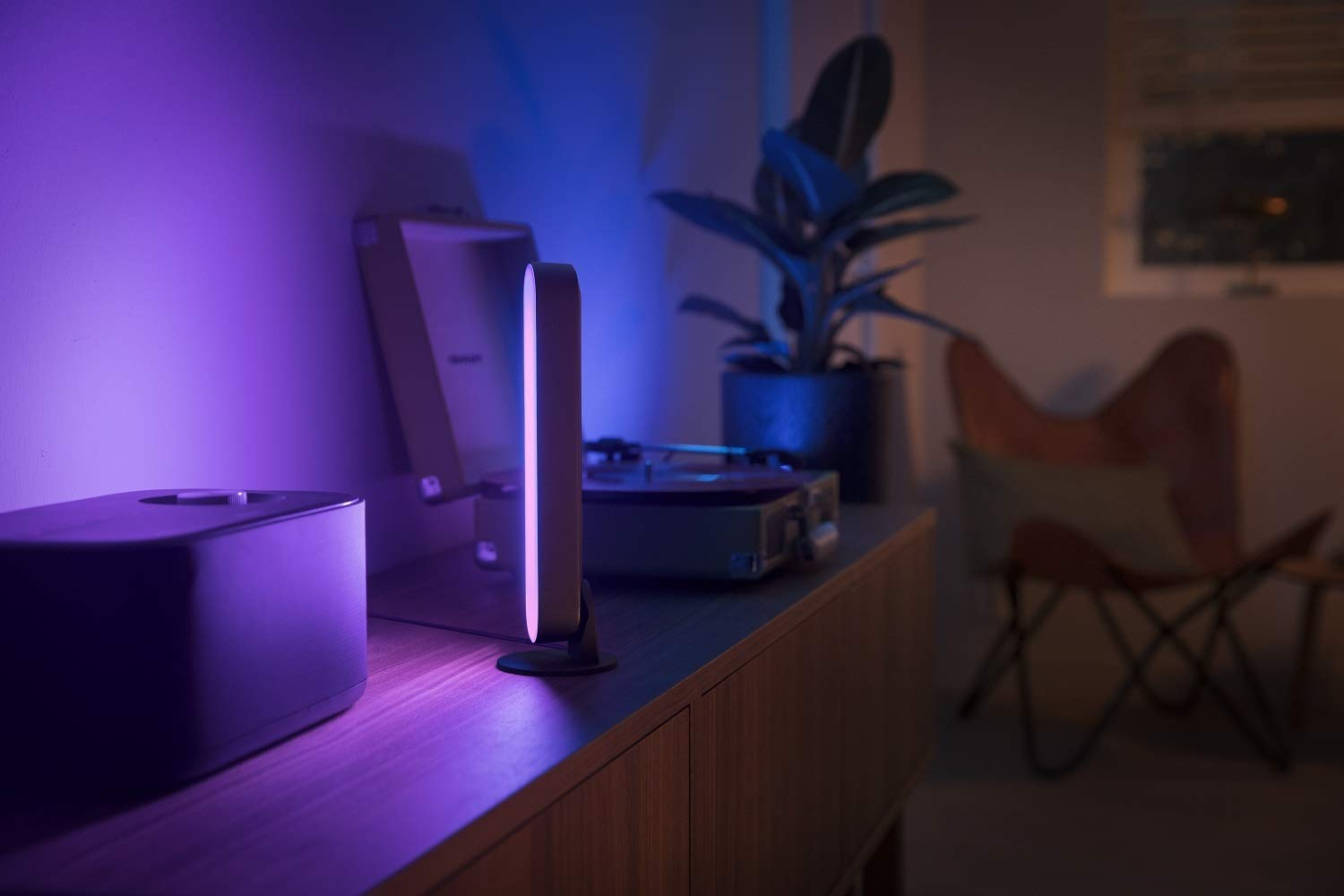 Una habitación con una lámpara morada, un tocadiscos, una planta y una silla.
