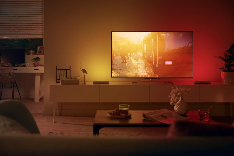 Una sala de estar con un televisor encendido. Una mujer camina en la pantalla del televisor.