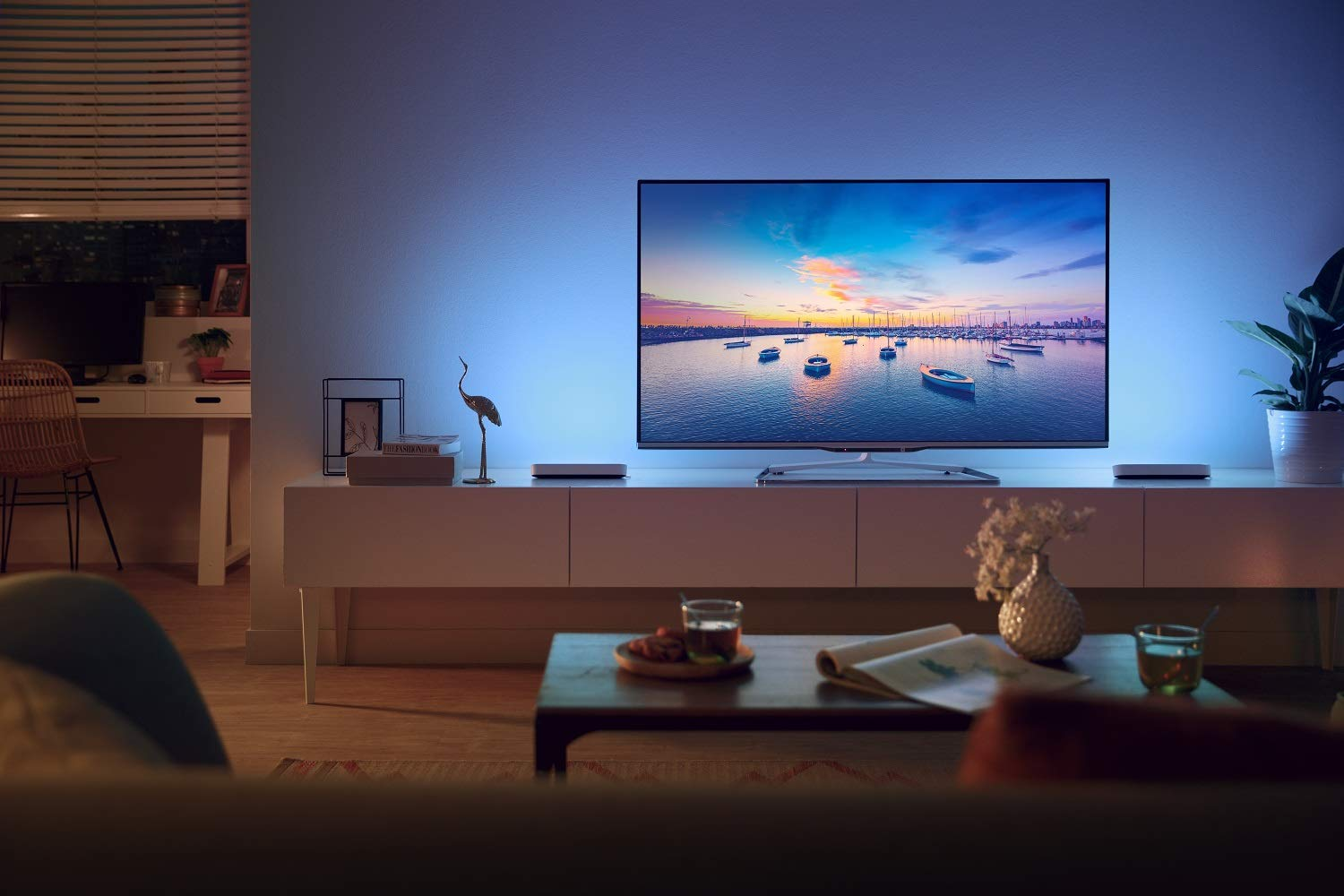 Salón con un televisor que muestra una escena de puerto. Un mueble blanco y un sofá en la escena.