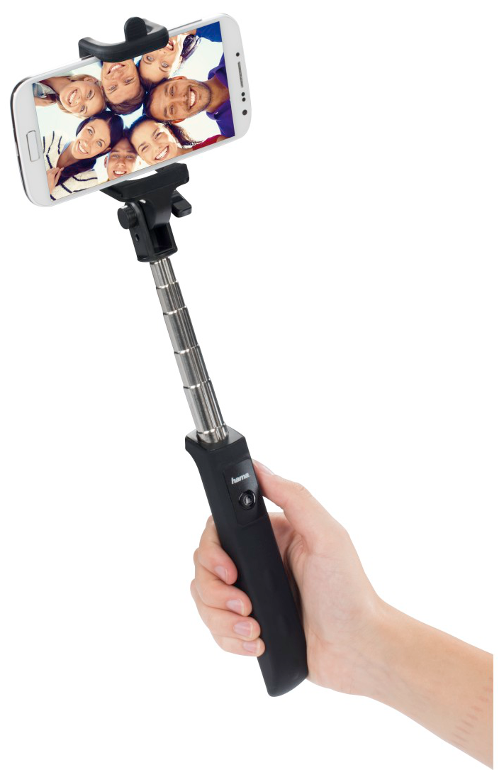 Una mano tiene un selfie stick con uno smartphone che mostra un gruppo di volti sorridenti.