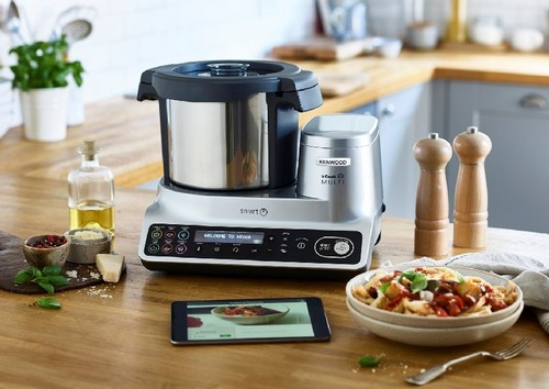 Electrodoméstico de cocina con comida en una mesa, con una tableta que muestra una receta.