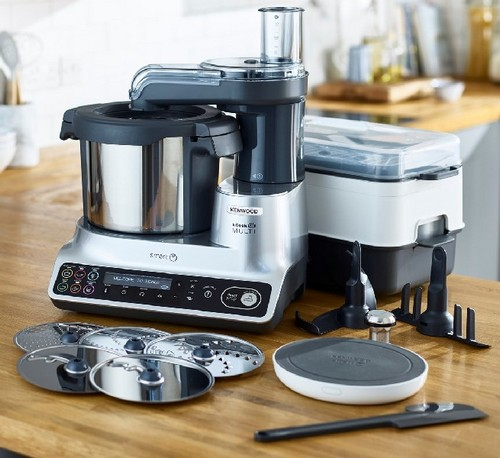 Procesador de alimentos Kenwood, plateado con múltiples accesorios, superficie de madera.