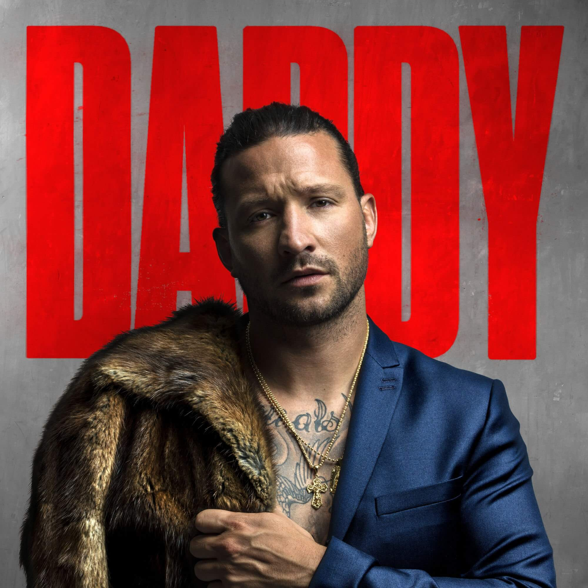 Un homme en costume bleu et manteau de fourrure, avec le mot 'DADDY' en rouge, sur fond gris.