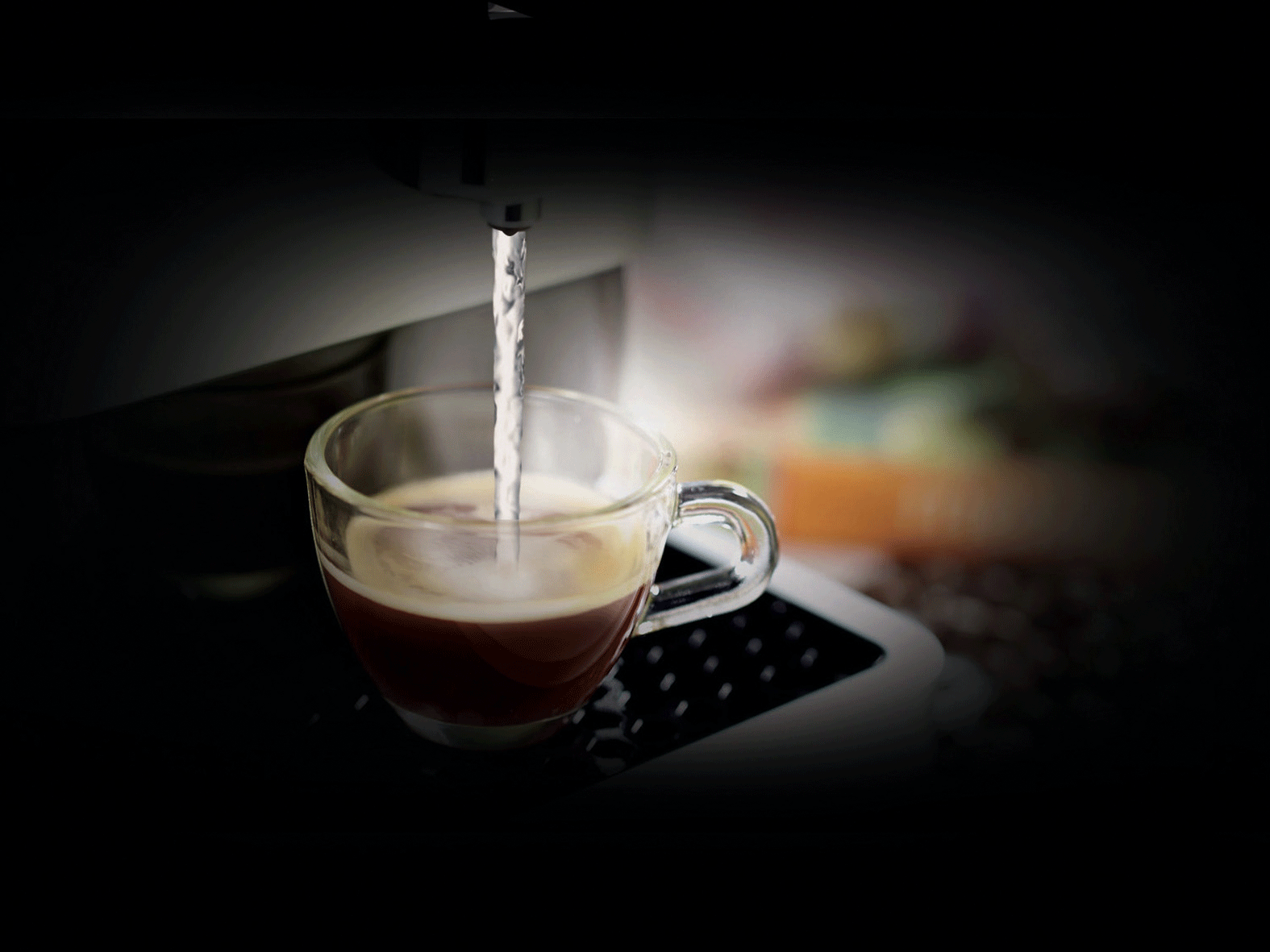 Ein Glas wird von einer Maschine mit Kaffee gefüllt. Wasserstrahl sichtbar.