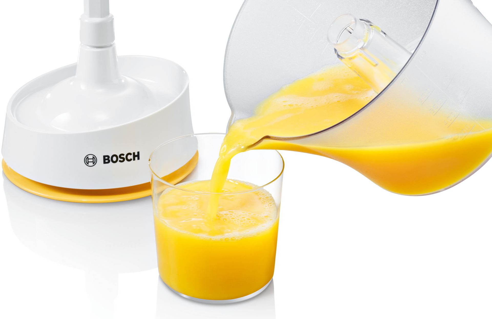 Jus d'orange versé d'un pichet transparent dans un verre à côté d'un presse-agrumes.