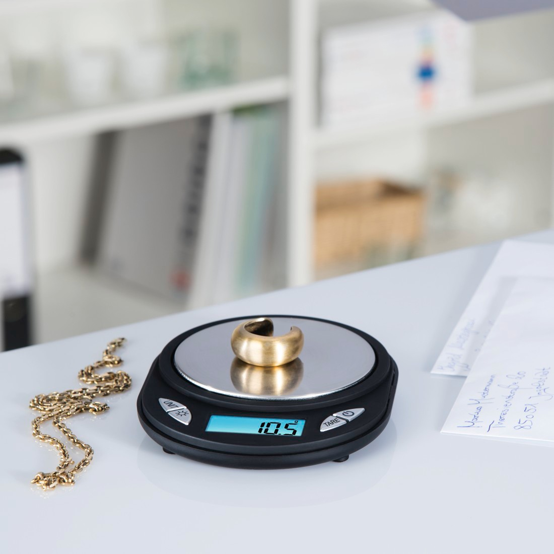 Goldring auf einer Waage mit Halskette und Papieren.