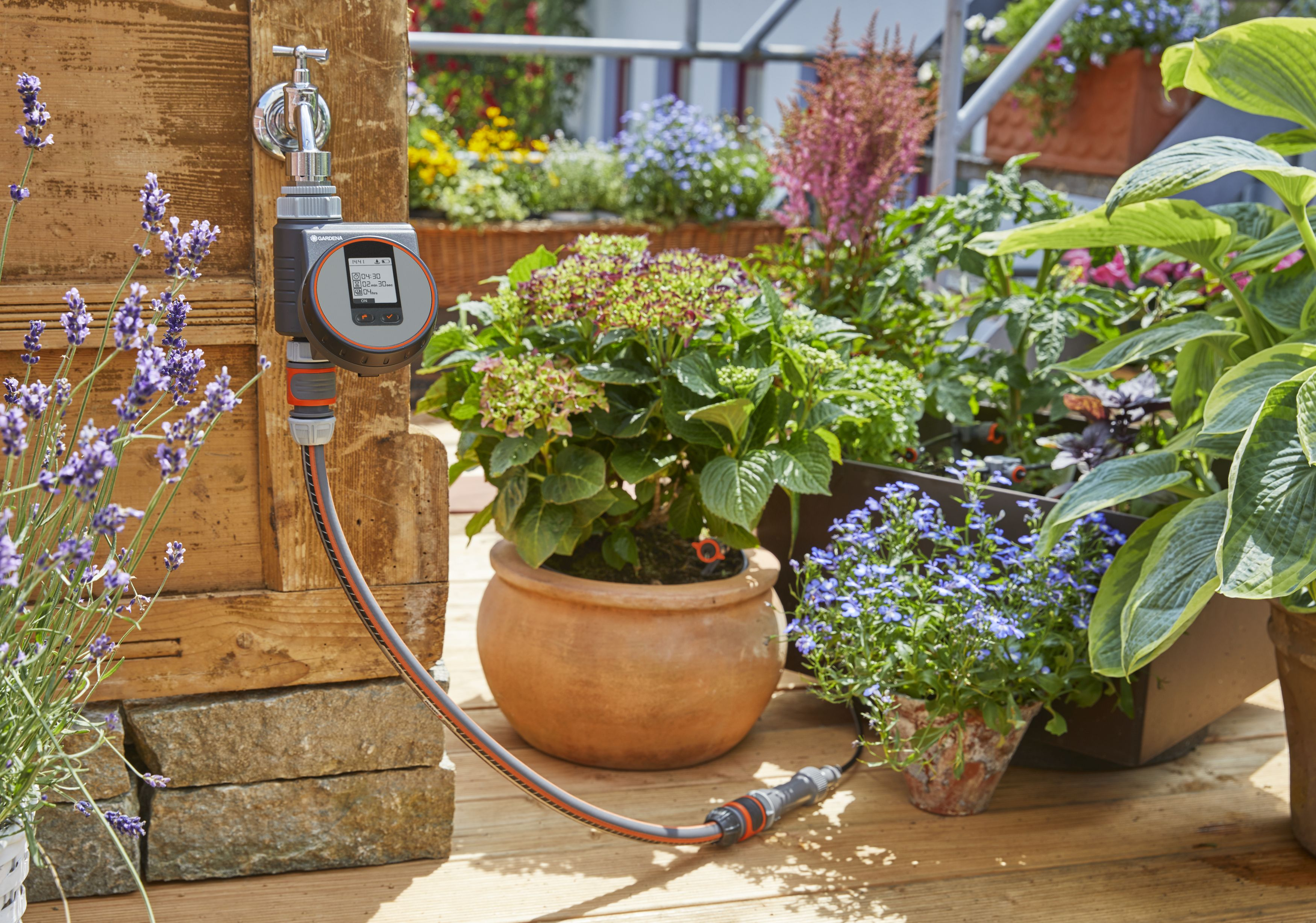 Ein Garten-Schlauch-Timer, der an einen Wasserhahn und einen Schlauch angeschlossen ist. Pflanzen umgeben es auf Holz.