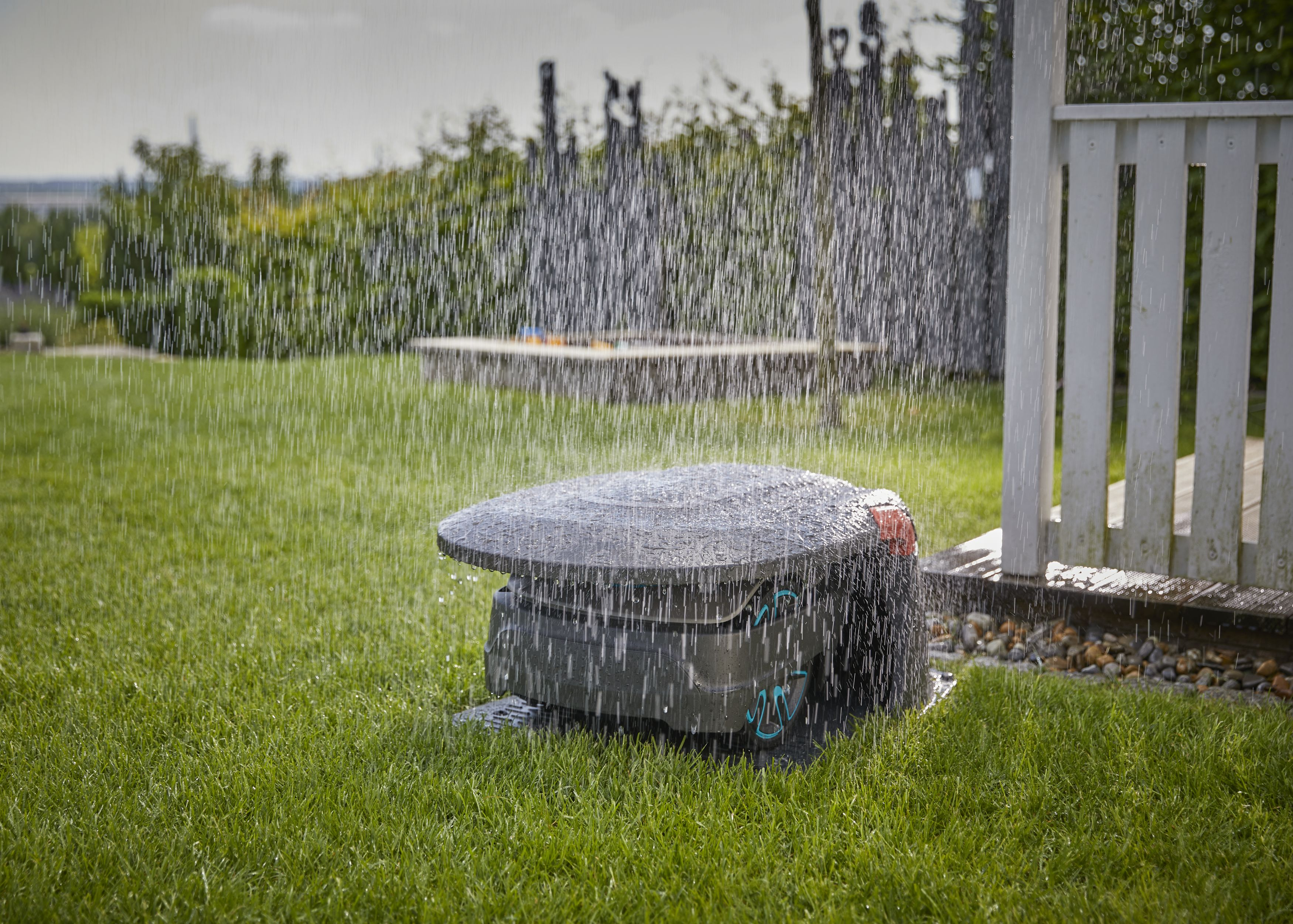 Rasenmäher in Aktion auf einem grünen Rasen, mit Wasser, das von oben sprüht.