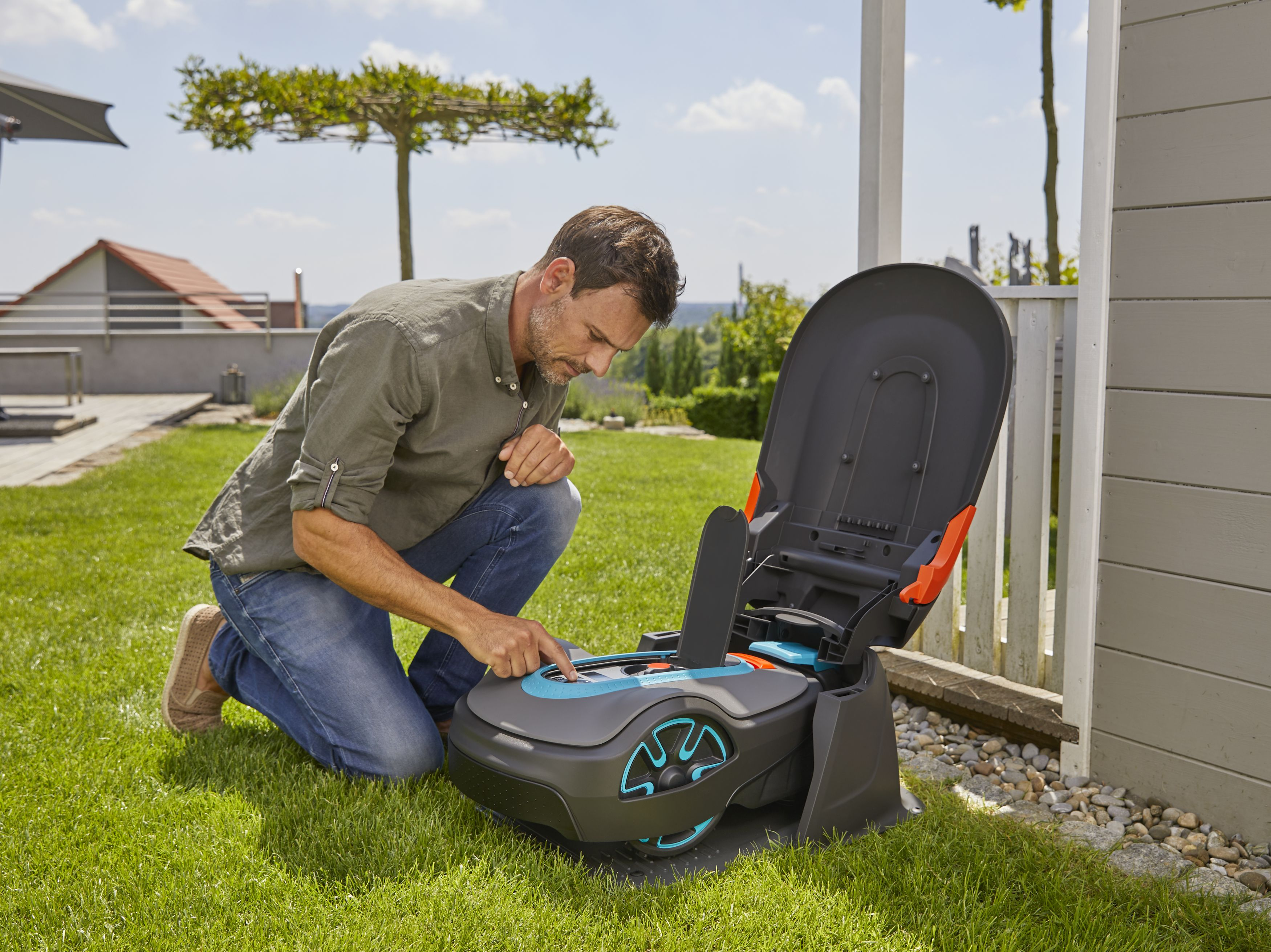 Mann inspiziert einen Roboter-Rasenmäher mit geöffnetem Deckel.