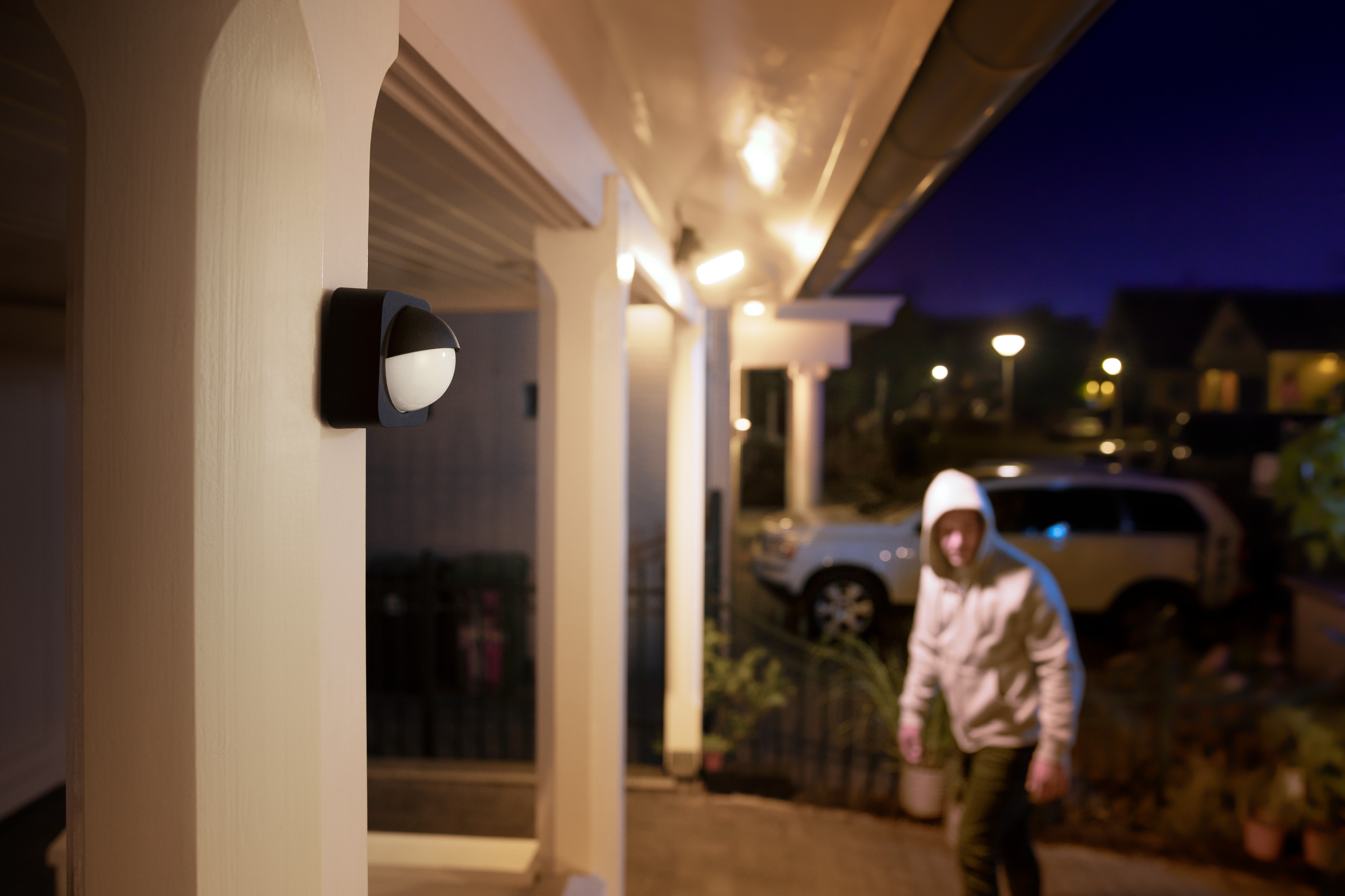 Ein Einbrecher mit Kapuzenpullover nähert sich einem Haus. Ein Licht an der Wand. Nachtszene.