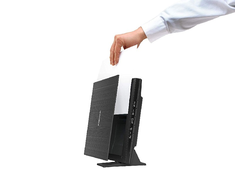 Una persona inserta un papel blanco en un escáner negro. El escáner está en posición vertical.