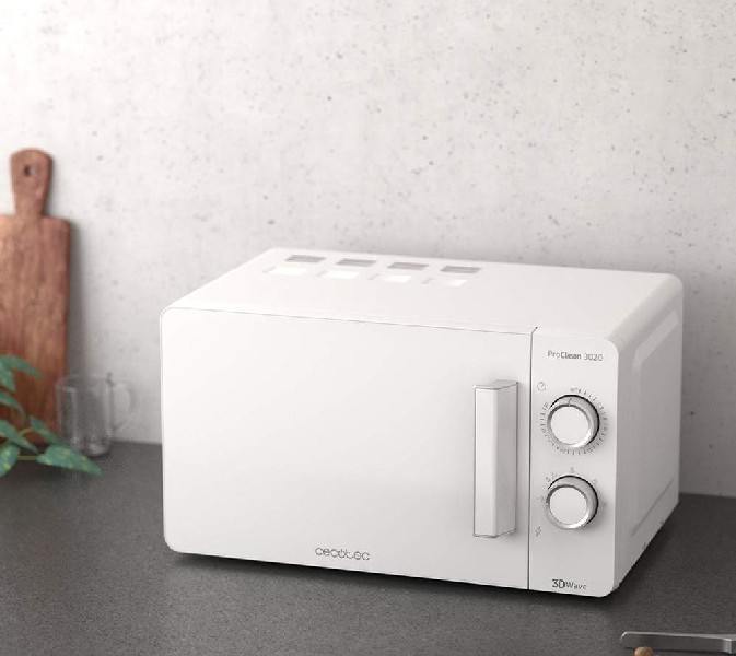 Un horno microondas blanco sobre una encimera con una tabla de cortar y tazas cerca.