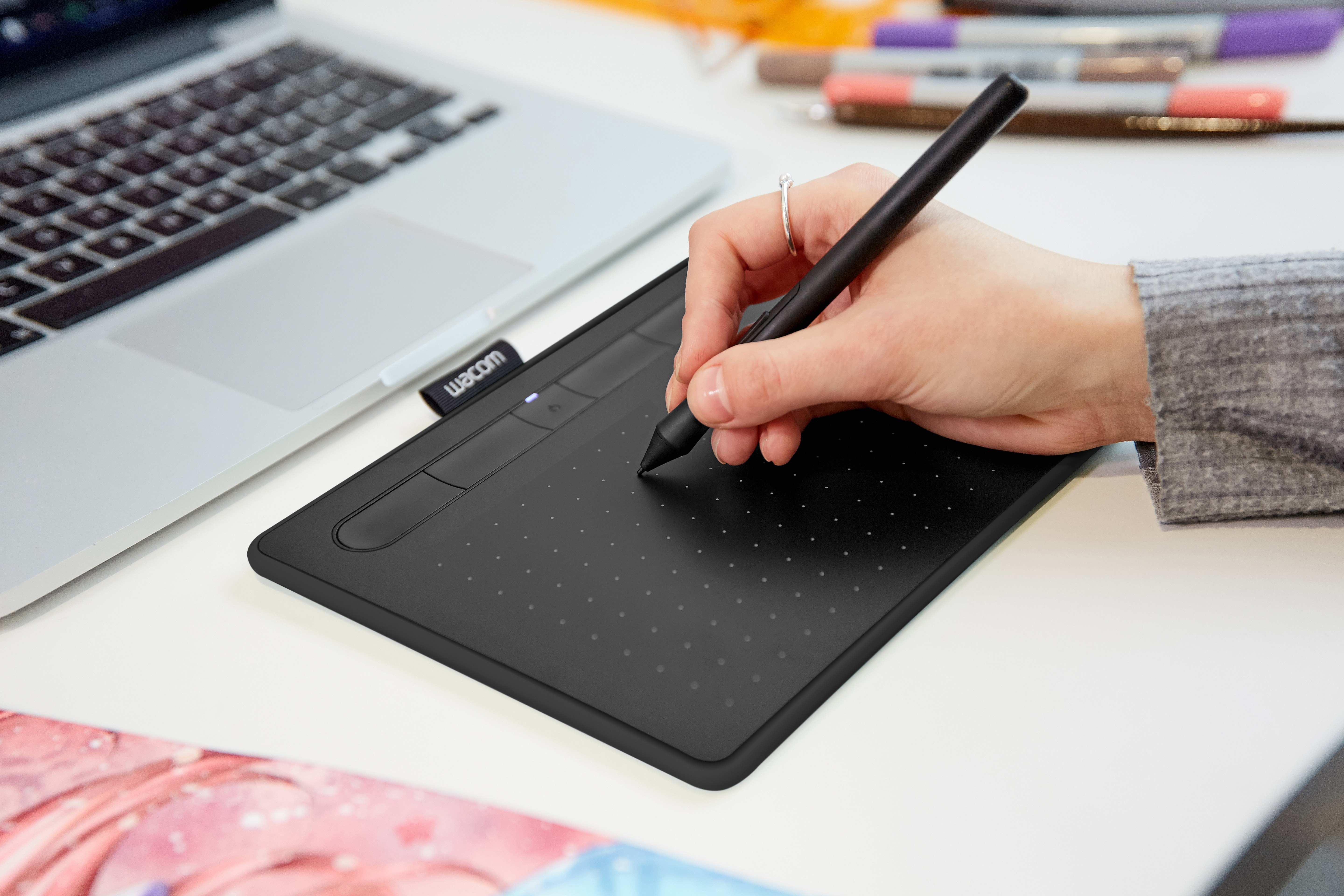 Person verwendet ein schwarzes Wacom-Tablet mit einem Laptop. Weißer Schreibtisch. Stift in der Hand.